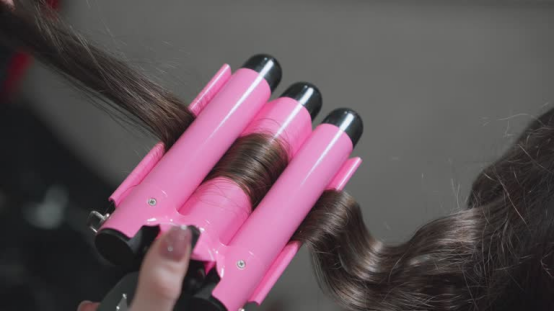 A pink triple-barrel heatless hair curler actively styling a section of hair, demonstrating its ease of use for creating voluminous waves on the go.